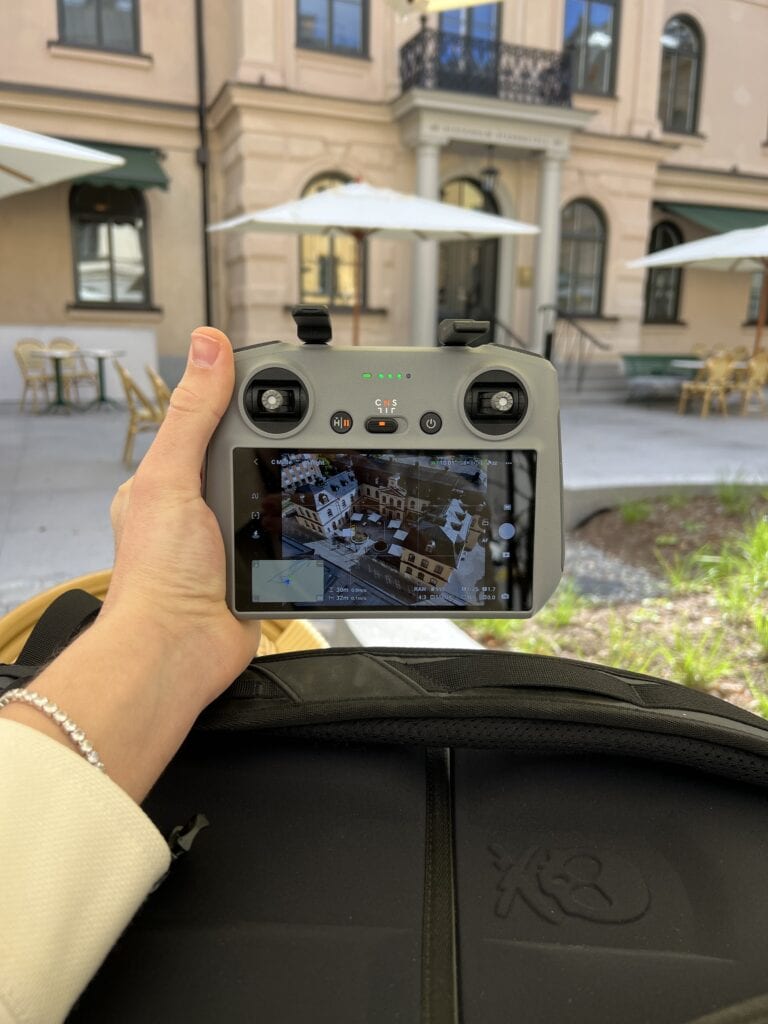 Fraymfulin dronelentäjä pitelee ohjainta Stockholm Stadshotellin sisäpihalla, ruudulla ilmakuva