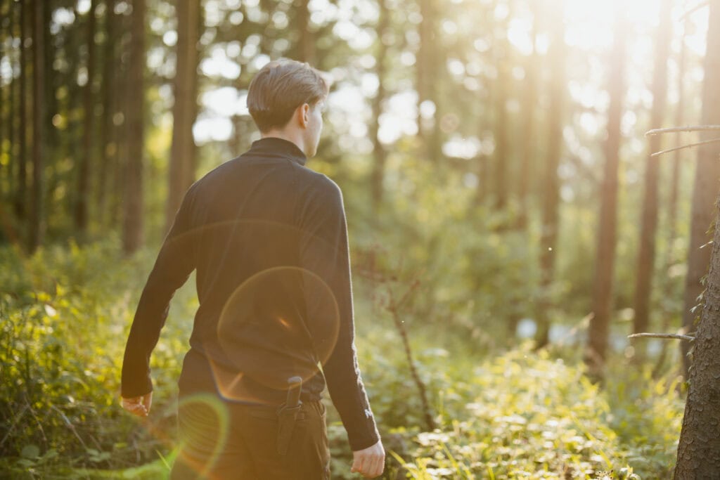 Malli yllään musta North Outdoorin merinovillapaita kävelee vastavaloiseen metsään Balingenissa Saksassa