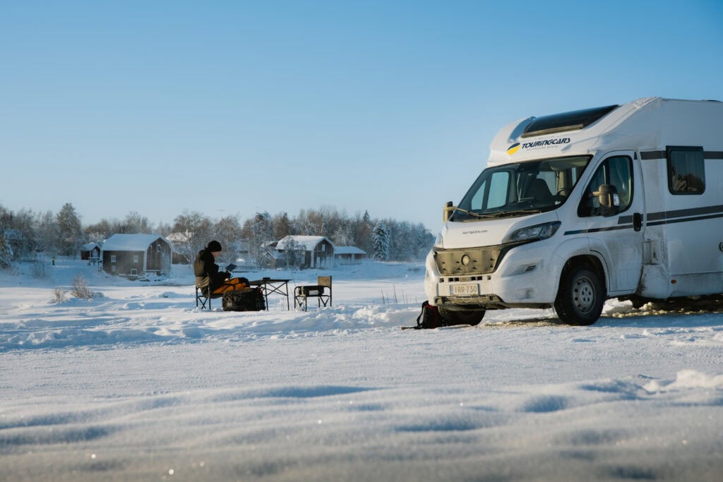 Ihminen istuu retkituolissa Touring Carsin matkailuauton vieressä lumikentällä Torniossa