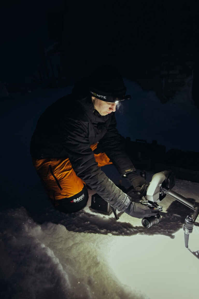 Fraymfulin videokuvaaja valmistelee dronea lumessa yöllä otsalampun valossa