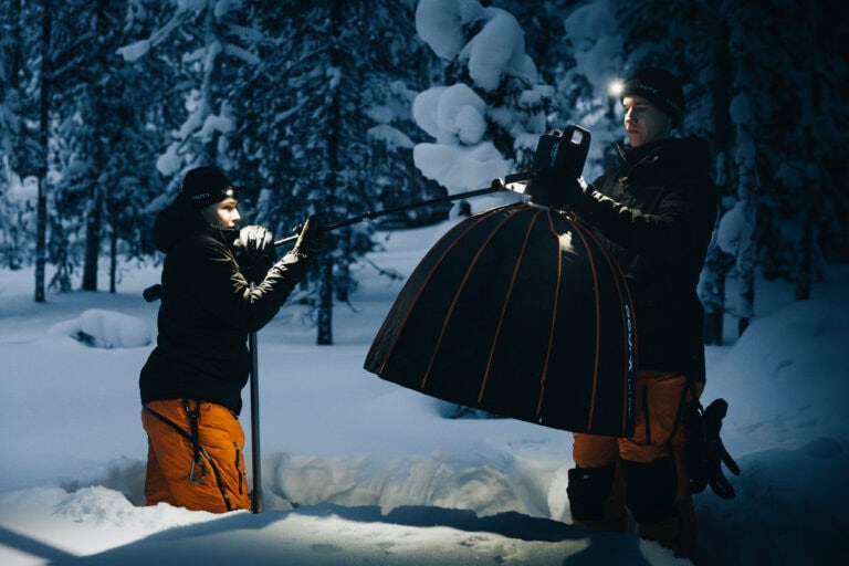 Kaksi kuvausryhmän jäsentä pystyttää softboxin ja puomimikrofonin lumisessa metsässä Ylläksellä