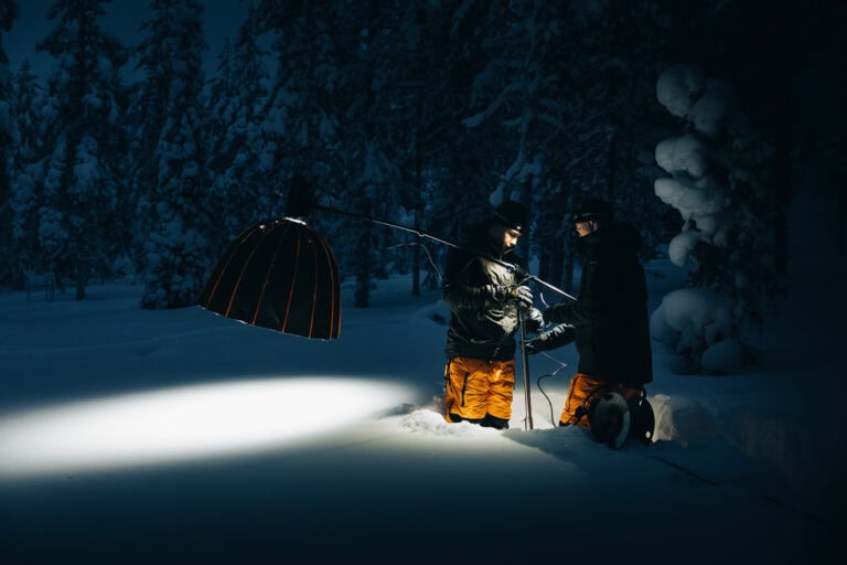 Kuvausryhmä valaisee lumista metsää softboxilla yöllä Lumoniten kuvauksissa Ylläksellä
