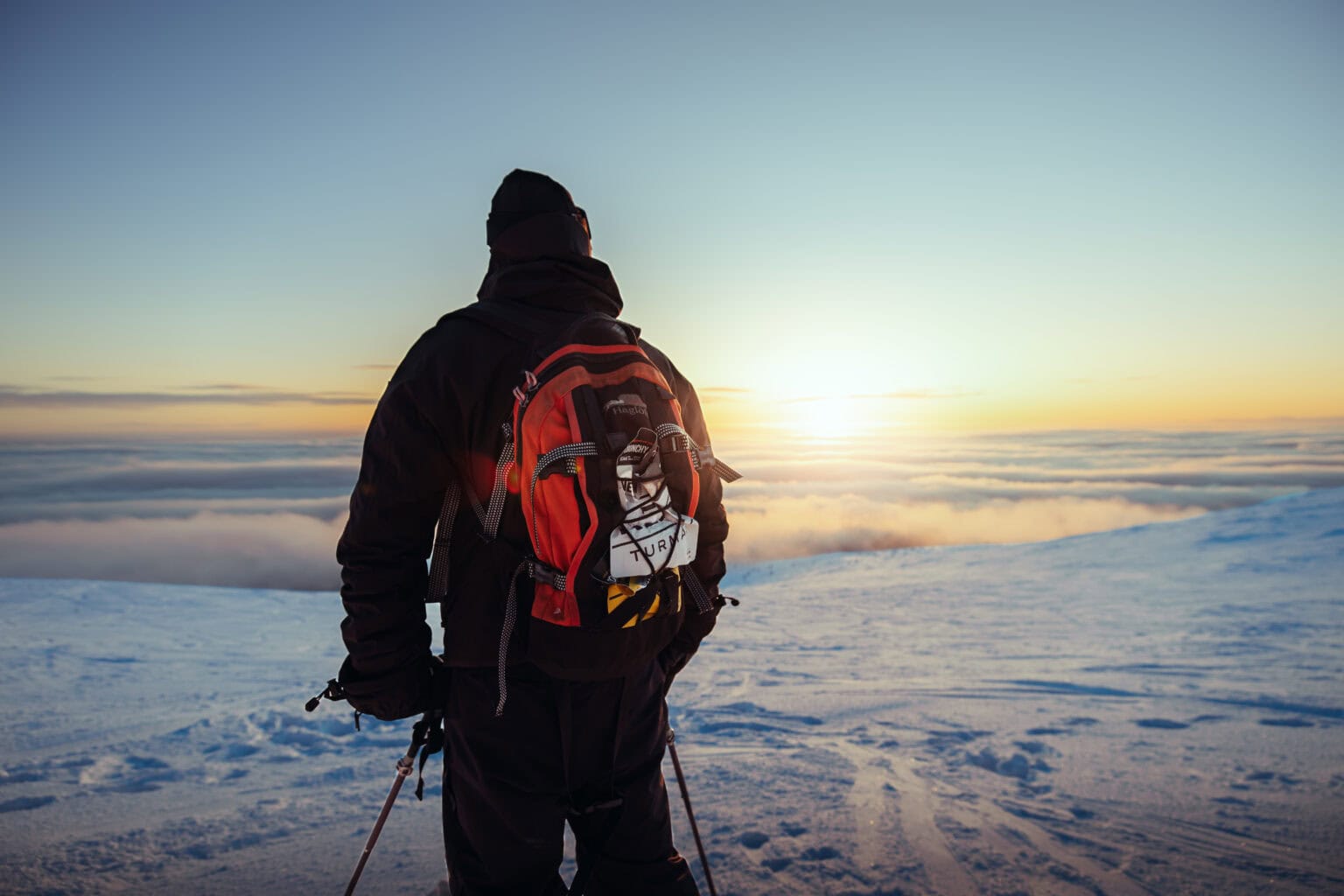 Splitboardaaja seisoo tunturissa auringonlaskussa pilvimeren yllä Ylläksellä