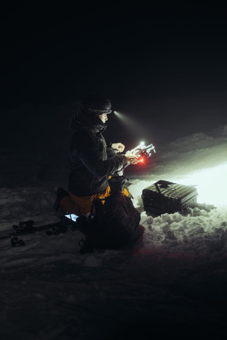 Dronelentäjä pitelee DJI Matricea yöllä, kalustolaukku ja sukset lumessa Ylläksellä