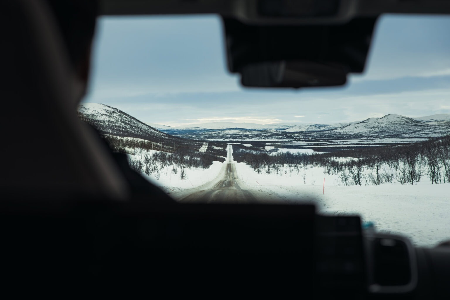 Näkymä matkailuauton tuulilasista suoralle tielle lumisten tunturien halki Kilpisjärvellä