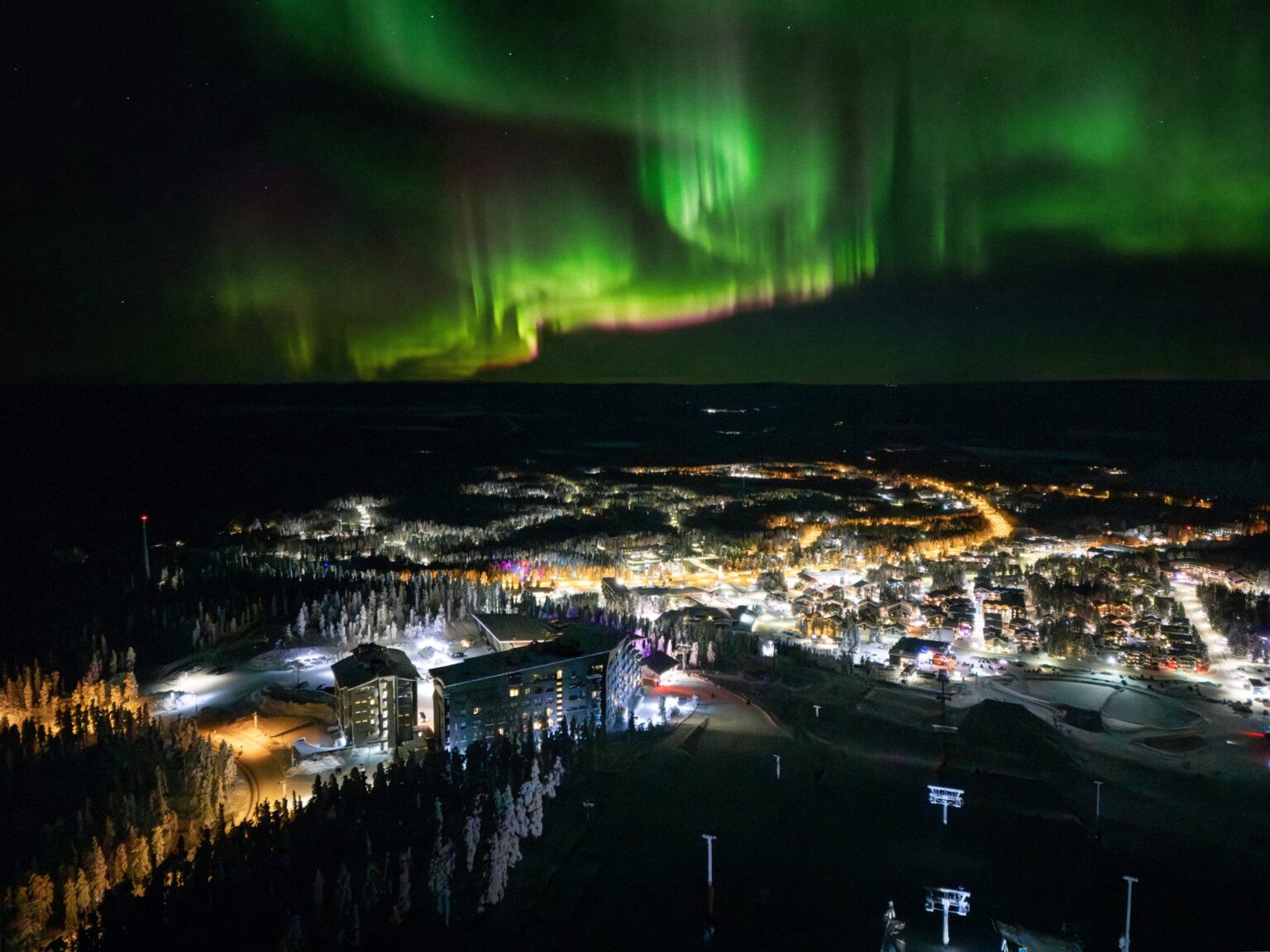 Revontulet Levin kylän yllä yöllä, etualalla valaistut Hotel Levi Panorama ja Levi Summit rinteellä