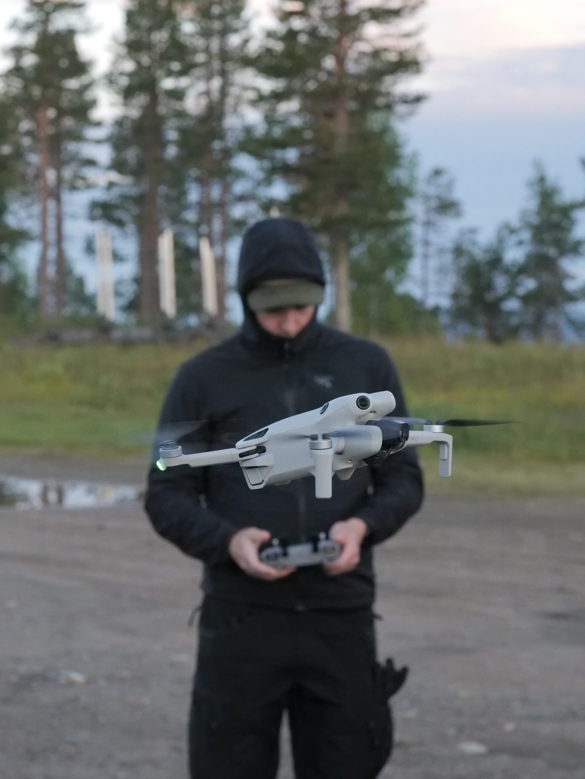 DJI Mini 4 Pro leijuu Fraymfulin dronelentäjän edessä, lentäjä pitelee kaukosäädintä valoisassa kesäyössä Levillä