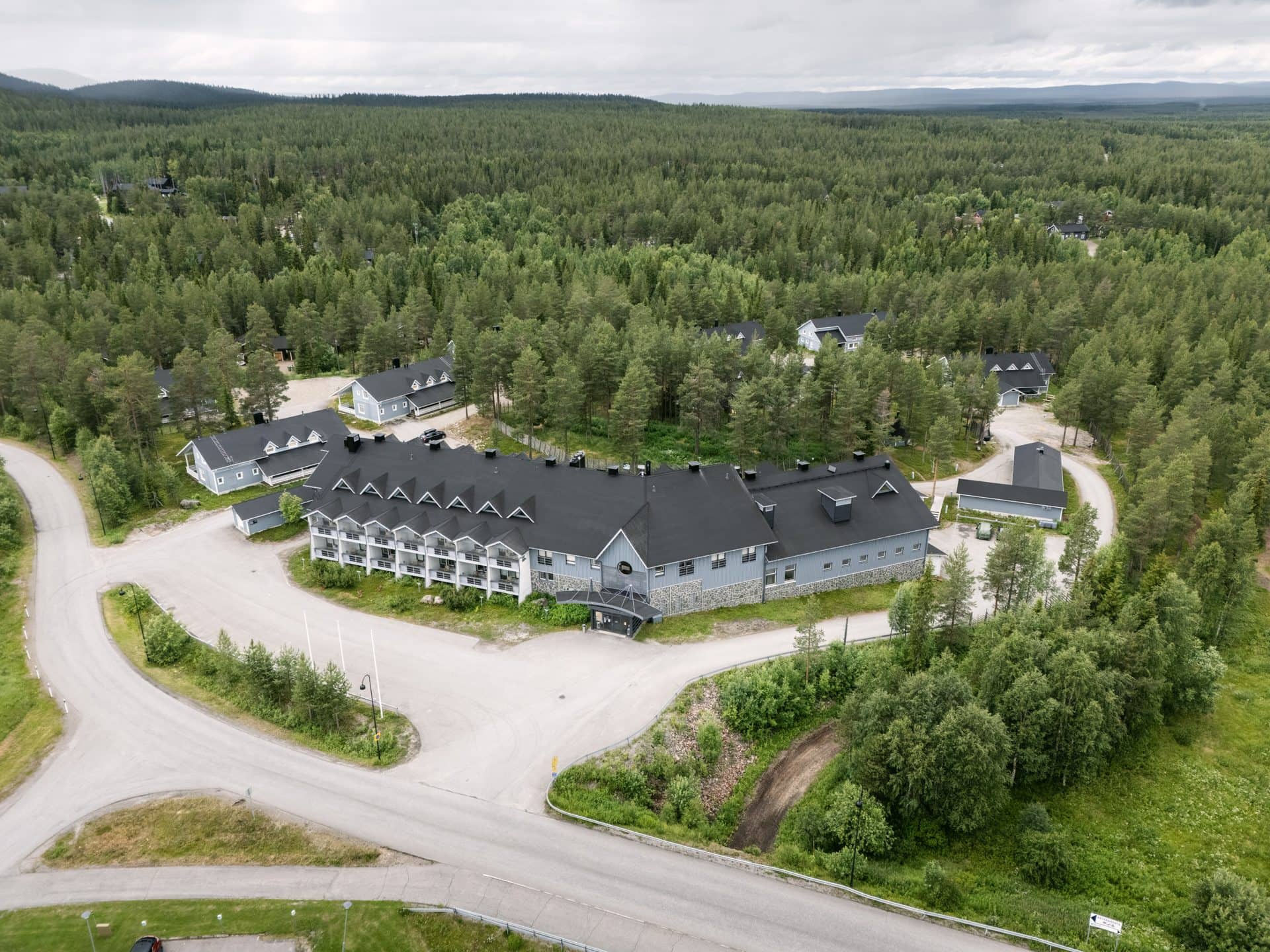 Hotel K5 Levi dronesta kesällä, pitkä rakennus tummalla harjakatolla mäntyjen keskellä