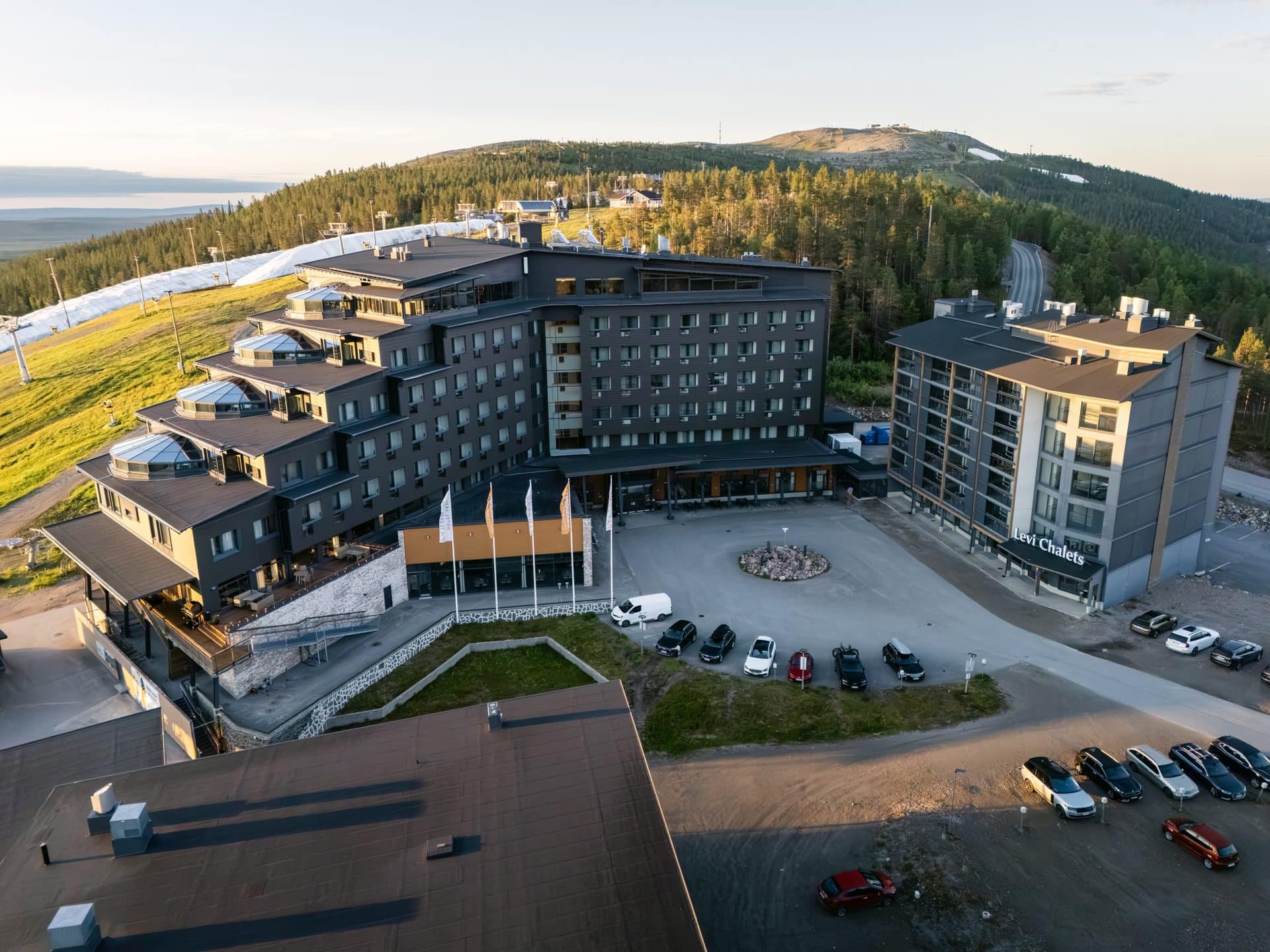 Hotel Levi Panoraman etusivu porrastetuilla lasikupolisviiteillä, lipputangot ja pysäköintialue