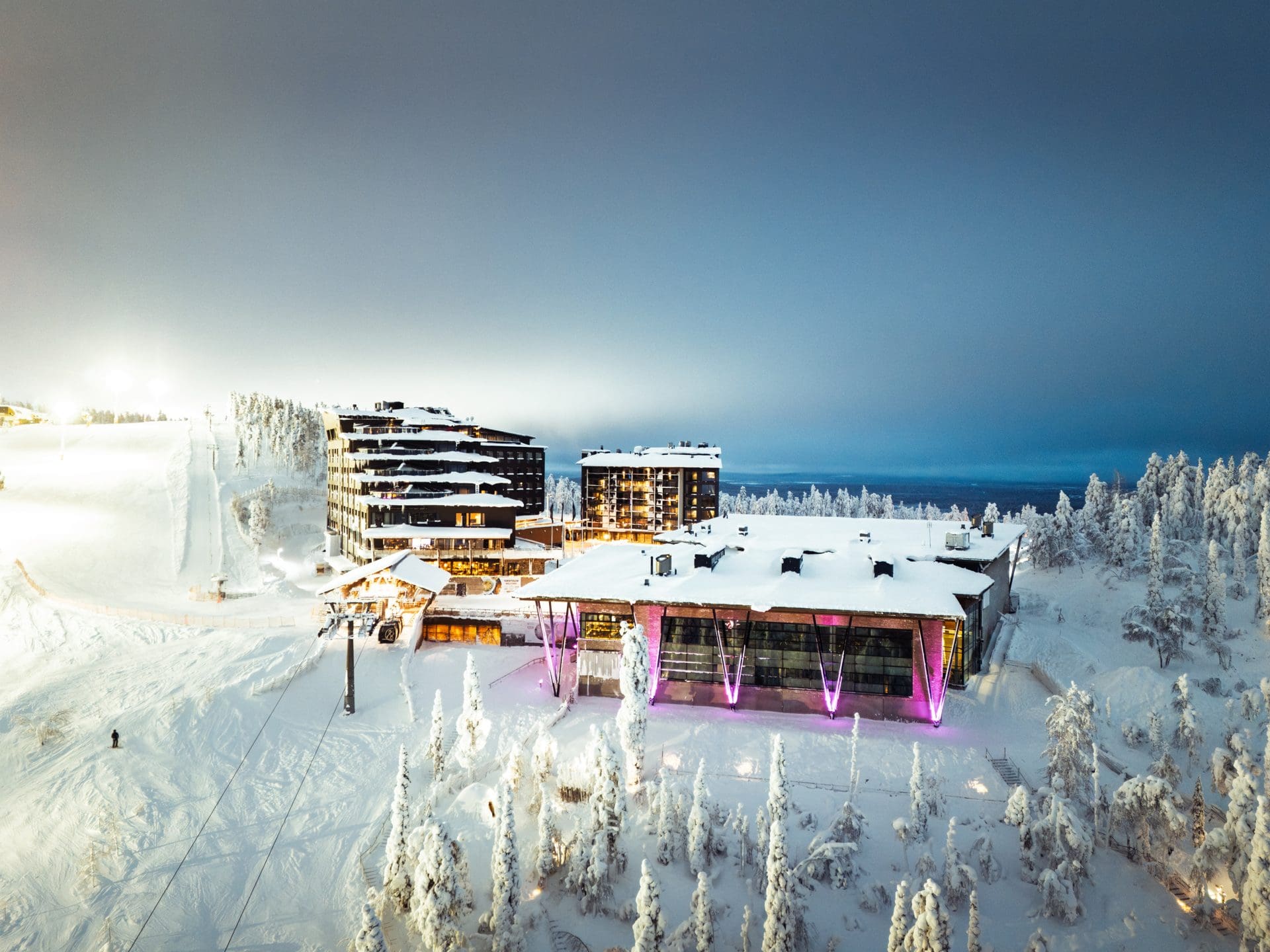 Levi Summit magentavaloissa sinisellä hetkellä, Hotel Levi Panorama takana lumisella rinteellä