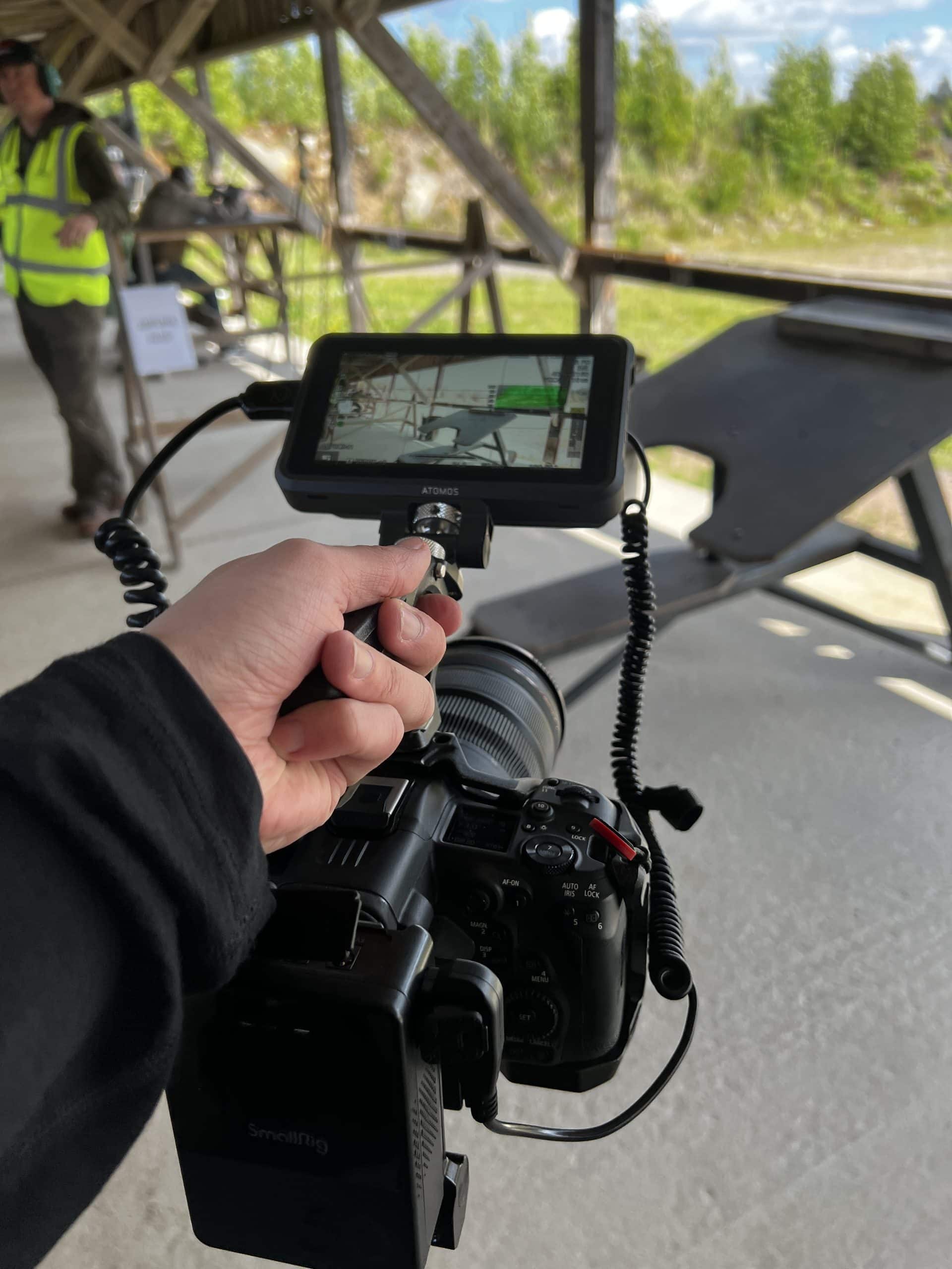 Käsi pitää Canon R5 C -runkoa, jonka päällä on Atomos-monitori, katetulla ampumapaikalla Erämessut Goes Rangessa Lopella.