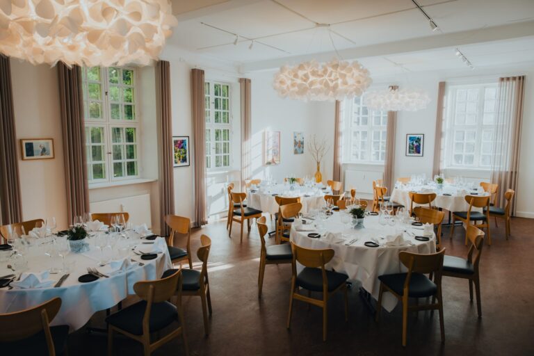 Valoisa ruokasali Augustenborg Gardenissa, pyöreät pöydät katettuina paperisten riippuvalaisimien alla