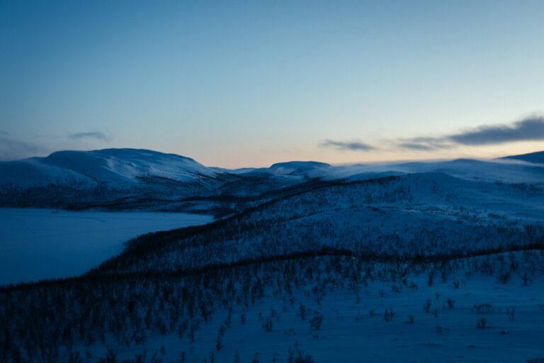 Lumisia tuntureita ja jäätynyt järvi sinisenä hetkenä Kilpisjärvellä, horisontissa viimeistä valoa