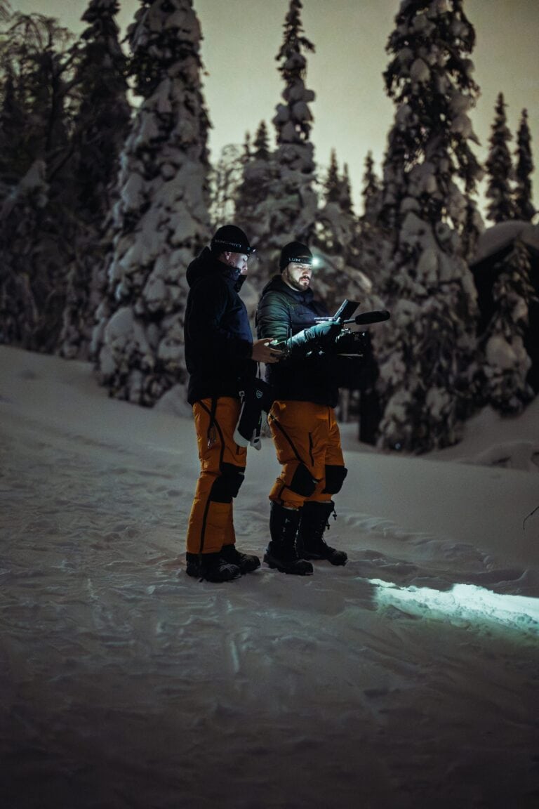 Kaksi Fraymfulin tekijää otsalampuissa tarkistaa kameraa lumisessa metsässä yöllä Ylläksellä
