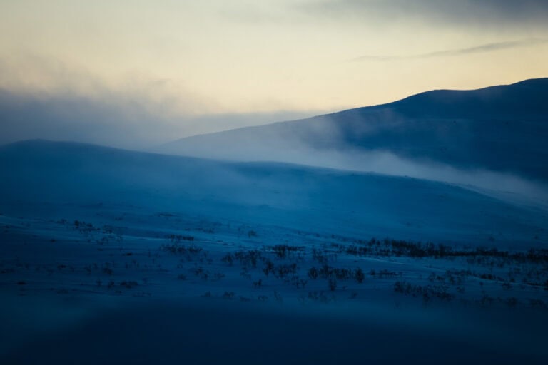 Usvaa lumisten tuntureiden yllä sinisenä hetkenä Kilpisjärvellä